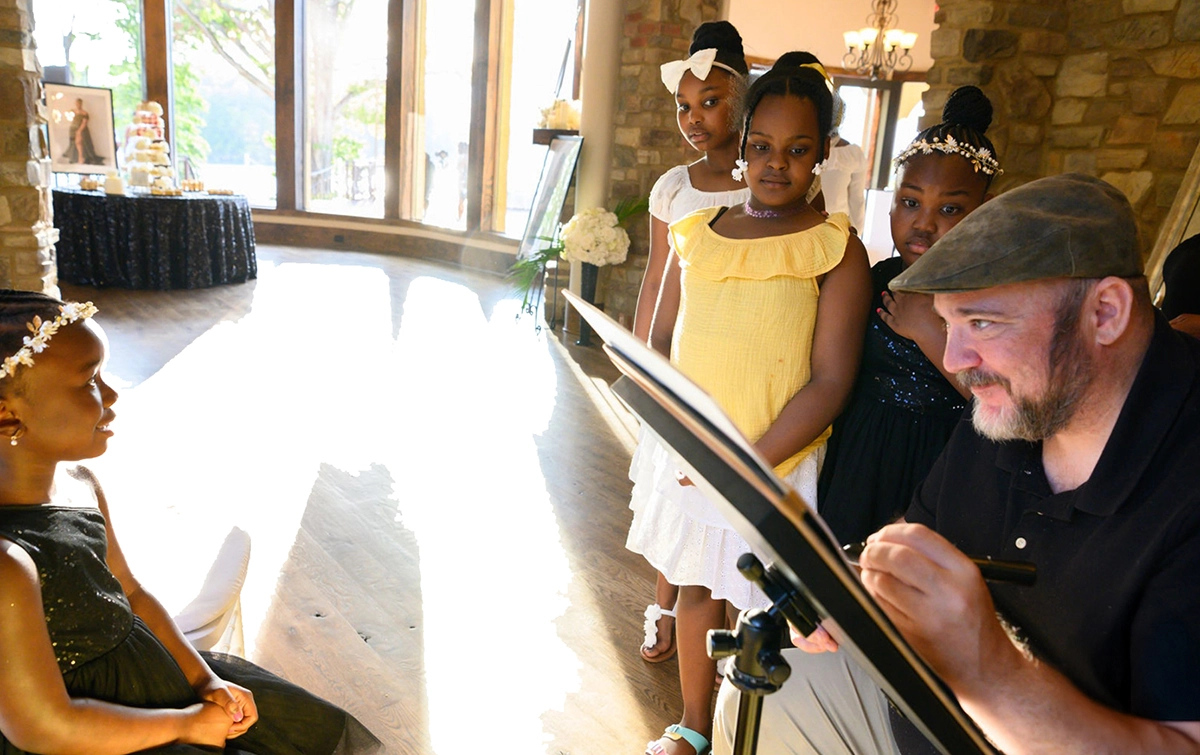 north carolina Caricaturist Eric Melton drawing Caricatures at a wedding while 3 black girls look on in admiration.